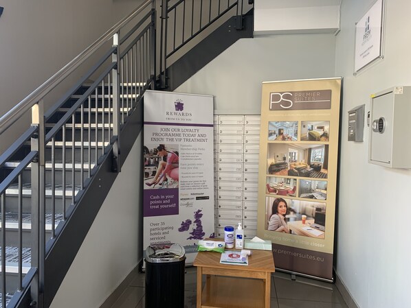 A hotel lobby with a staircase, a loyalty rewards poster, a security kiosk, and a table with toiletries. - PREMIER SUITES Birmingham (Birmingham)