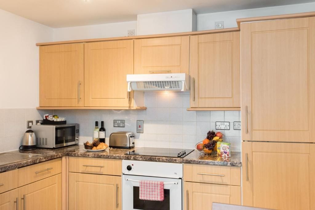 Een keuken met houten kastjes, een magnetron, een broodrooster en een fornuis.