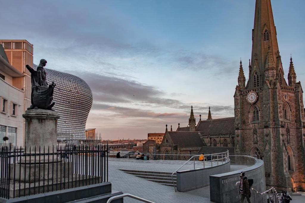 A city square with a statue, a modern building, and a historic church.