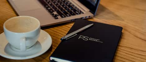A laptop, a cup of coffee, and a notebook on a wooden table.