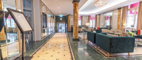 Un vestíbulo de hotel con piso de mármol, una recepción, zona de estar y grandes ventanales.
