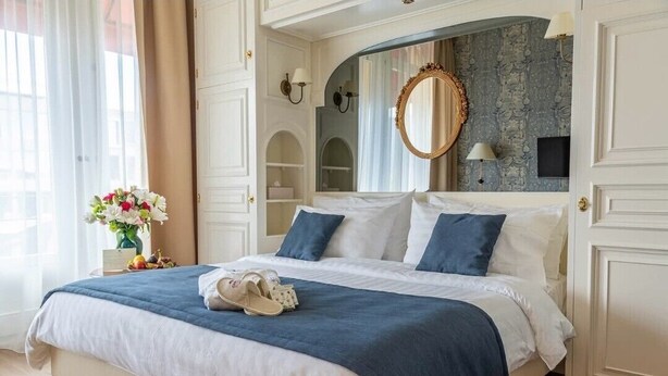 Une chambre d’hôtel avec un grand lit, un miroir, un vase de fleurs et une vue sur la ville.