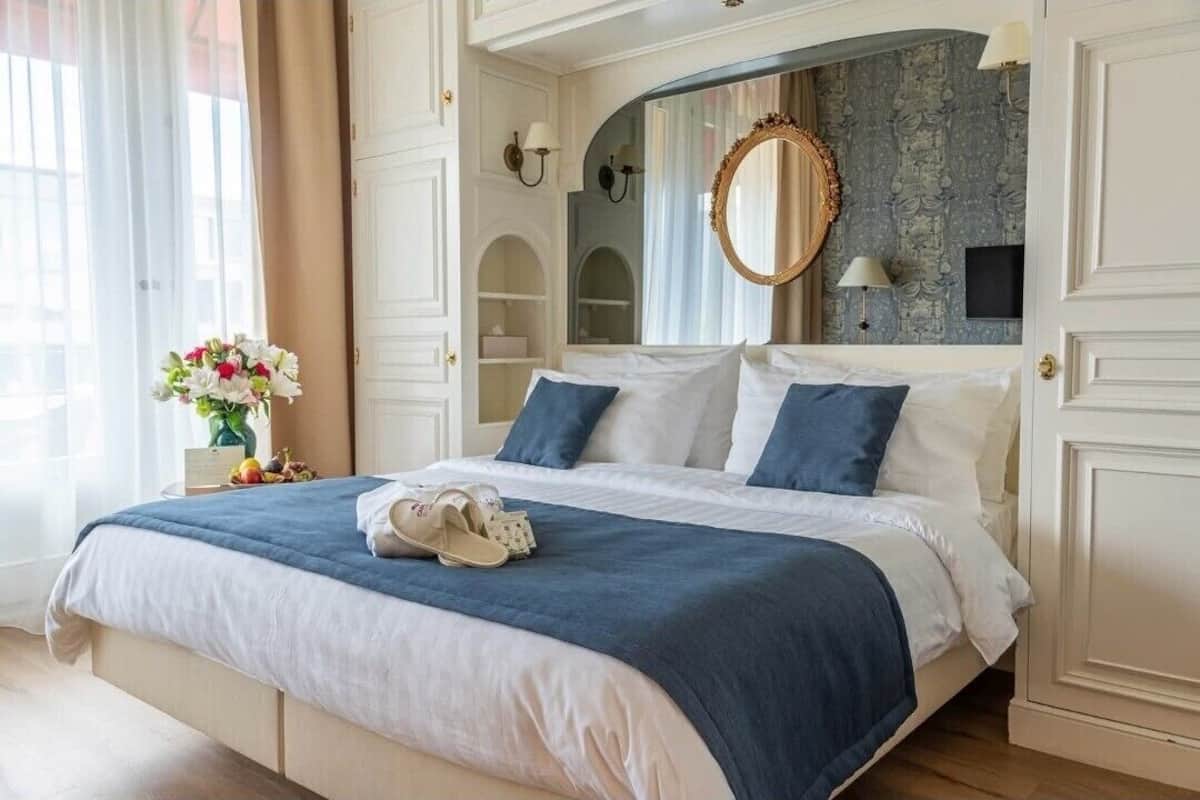 A hotel room with a large bed, a mirror, a vase of flowers, and a view of the city.