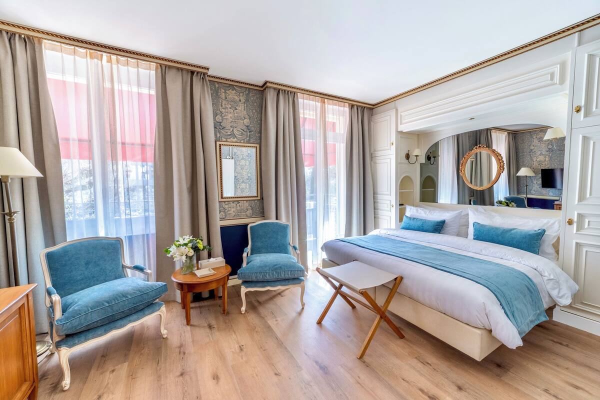 A bedroom with a bed, two armchairs, a small table, and a mirror.