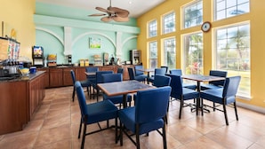 Ein Restaurant mit blauen Stühlen und Tischen, einer Küchenzeile und großen Fenstern.
