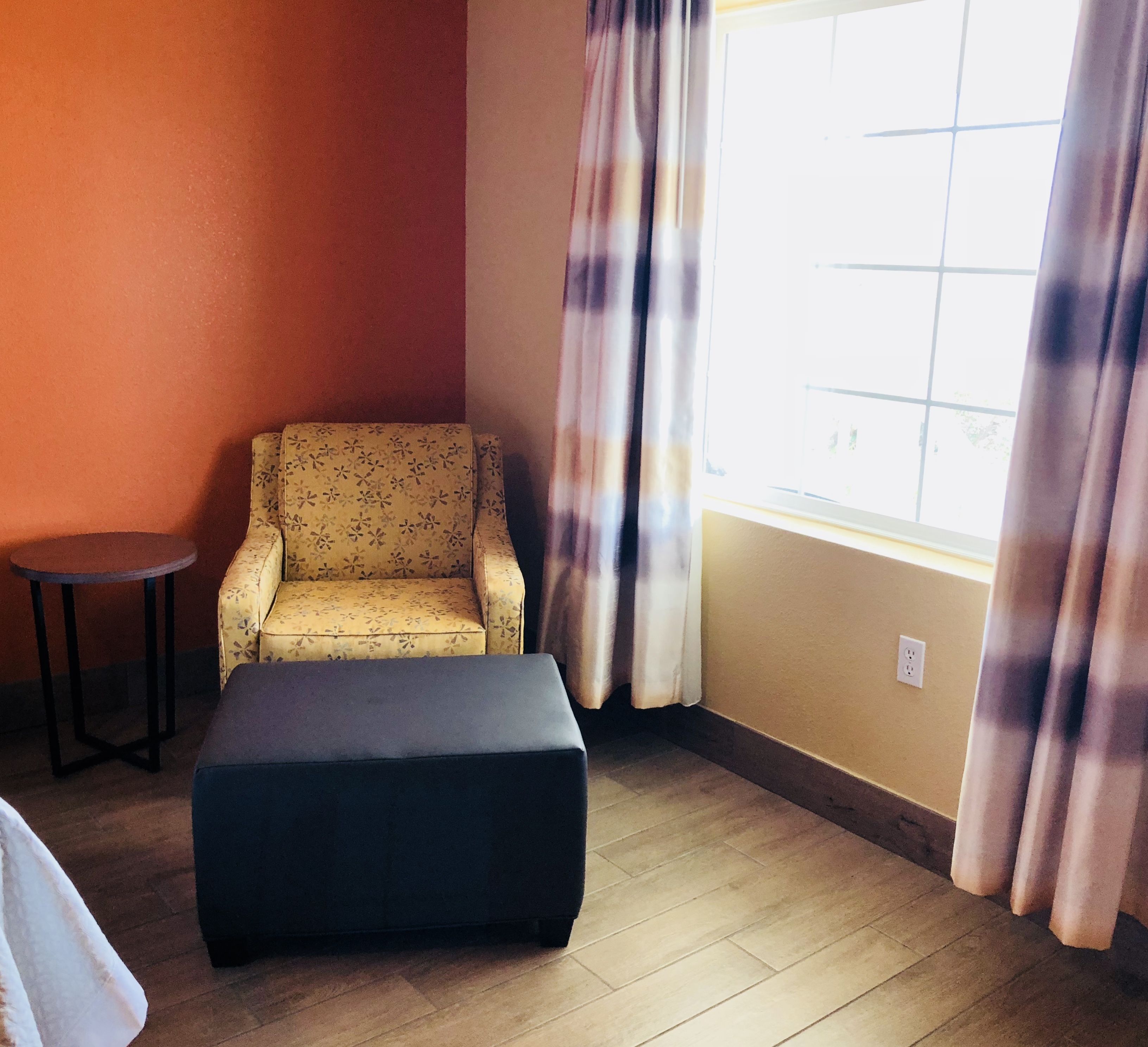 A room with a patterned armchair, a small round table, and a black ottoman.