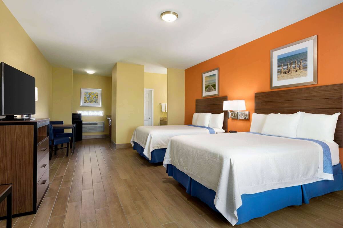 Een hotelkamer met twee bedden, een bureau, een televisie en een raam met uitzicht op het strand.