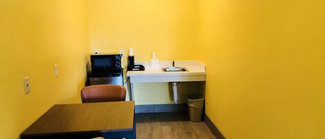 A small kitchenette with a microwave, coffee maker, and sink. There is a wooden table and two chairs.