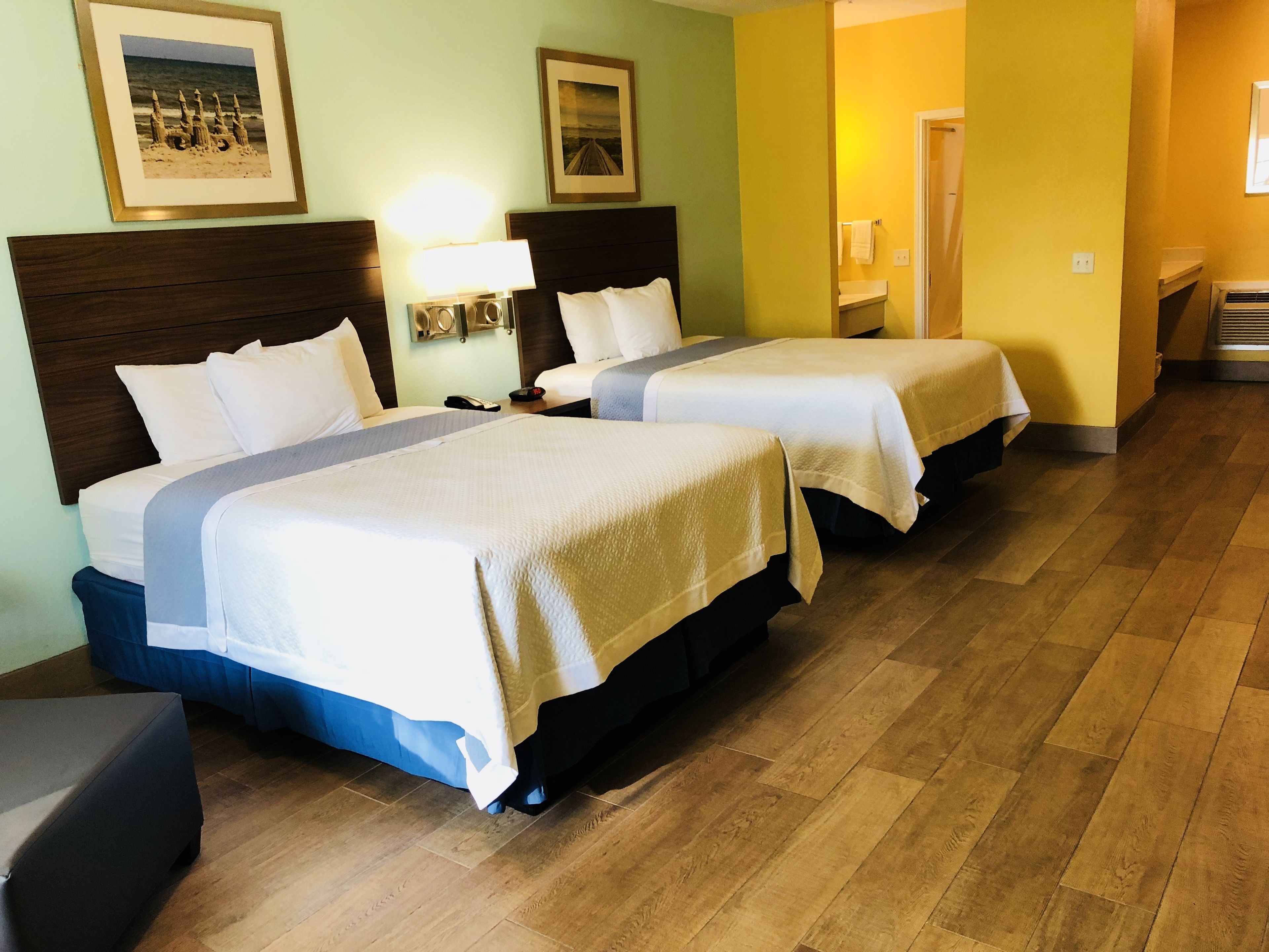 A hotel room with two beds, a nightstand, a lamp, and a framed picture on the wall.