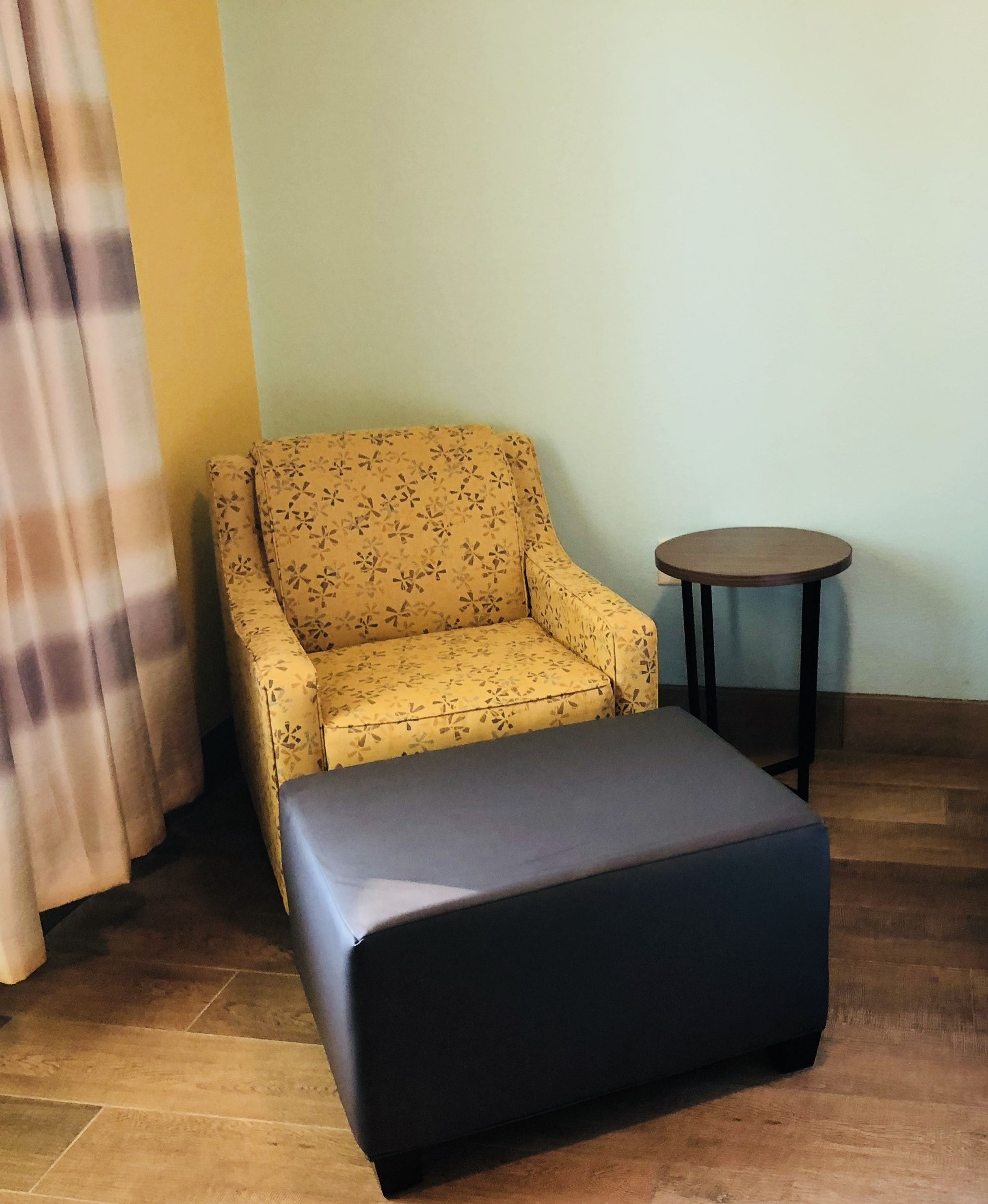 A room with a yellow floral sofa, a small round table, and a black ottoman.