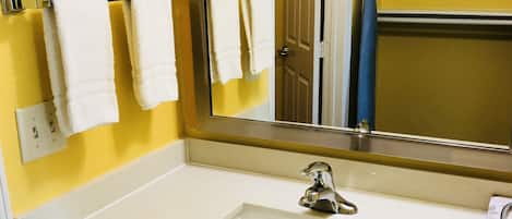 A bathroom with a white sink, a mirror, and a towel rack with white towels.