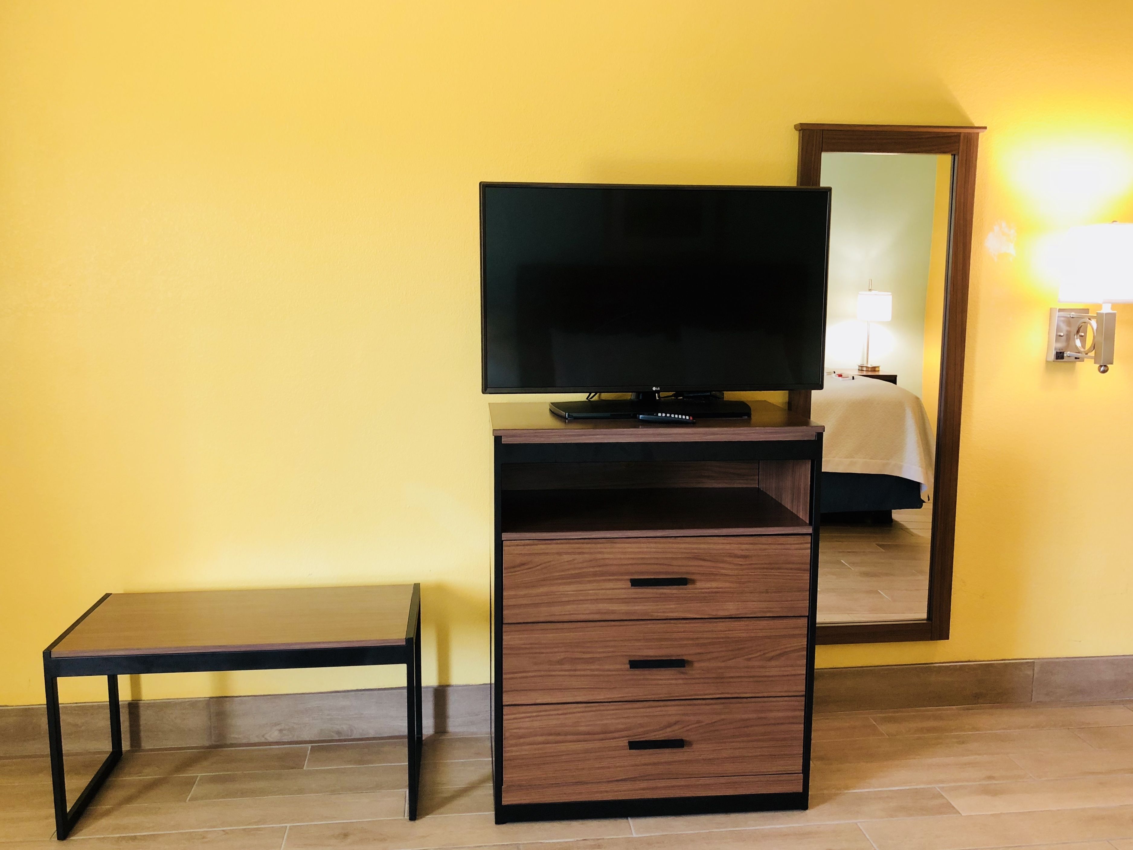 Una habitación con televisión sobre un mueble de madera, una mesita y un espejo en la pared.
