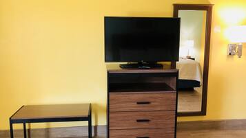 Una habitación con televisión sobre un mueble de madera, una mesita y un espejo en la pared.