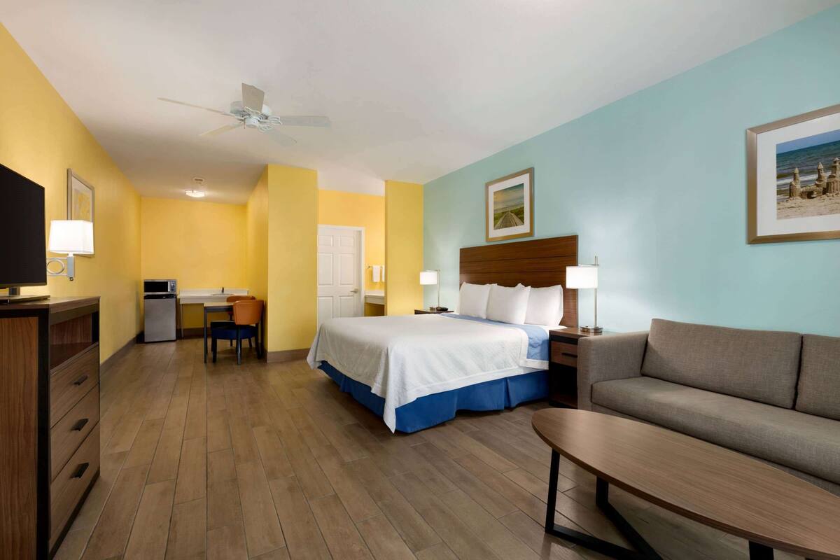 Een hotelkamer met een bed, een bank, een bureau, een televisietoestel en een plafondventilator.