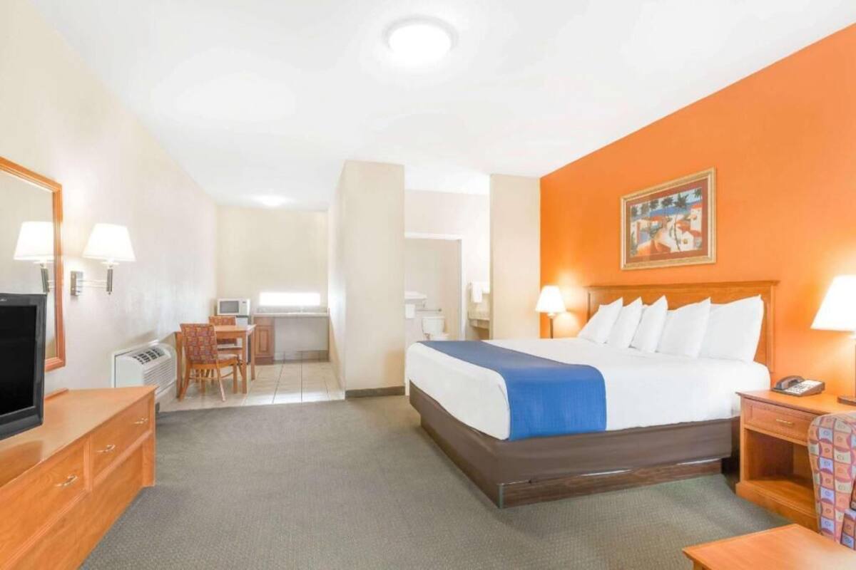Een hotelkamer met een bed, bureau, stoel, televisie en een schilderij aan de muur.