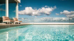 A clear swimming pool with lounge chairs and a glass railing overlooking a cityscape. - be.HOTEL (St. Julian's)