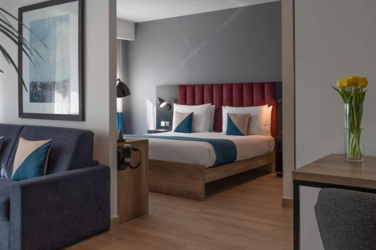 A modern hotel room with a bed, a sofa, a desk, and a chair.