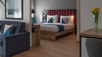 A modern hotel room with a bed, a sofa, a desk, and a chair.