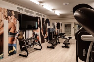 A gym with exercise equipment, a TV, and motivational posters on the walls.