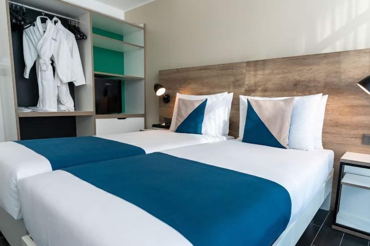 A hotel room with two beds, a wardrobe, and a nightstand.