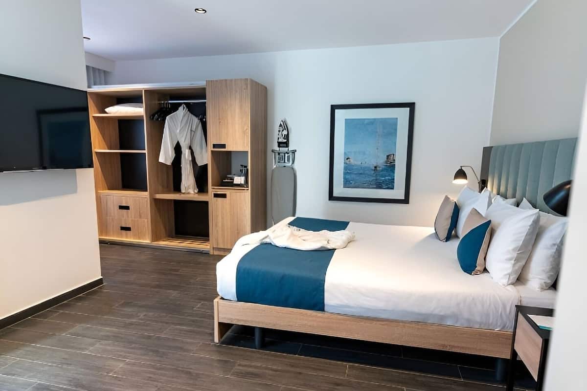 A modern hotel room with a bed, a wardrobe, a TV, and a framed picture on the wall.