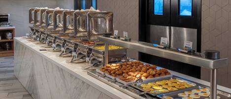 A buffet setup with various food stations, including trays of eggs, pastries, and other items.