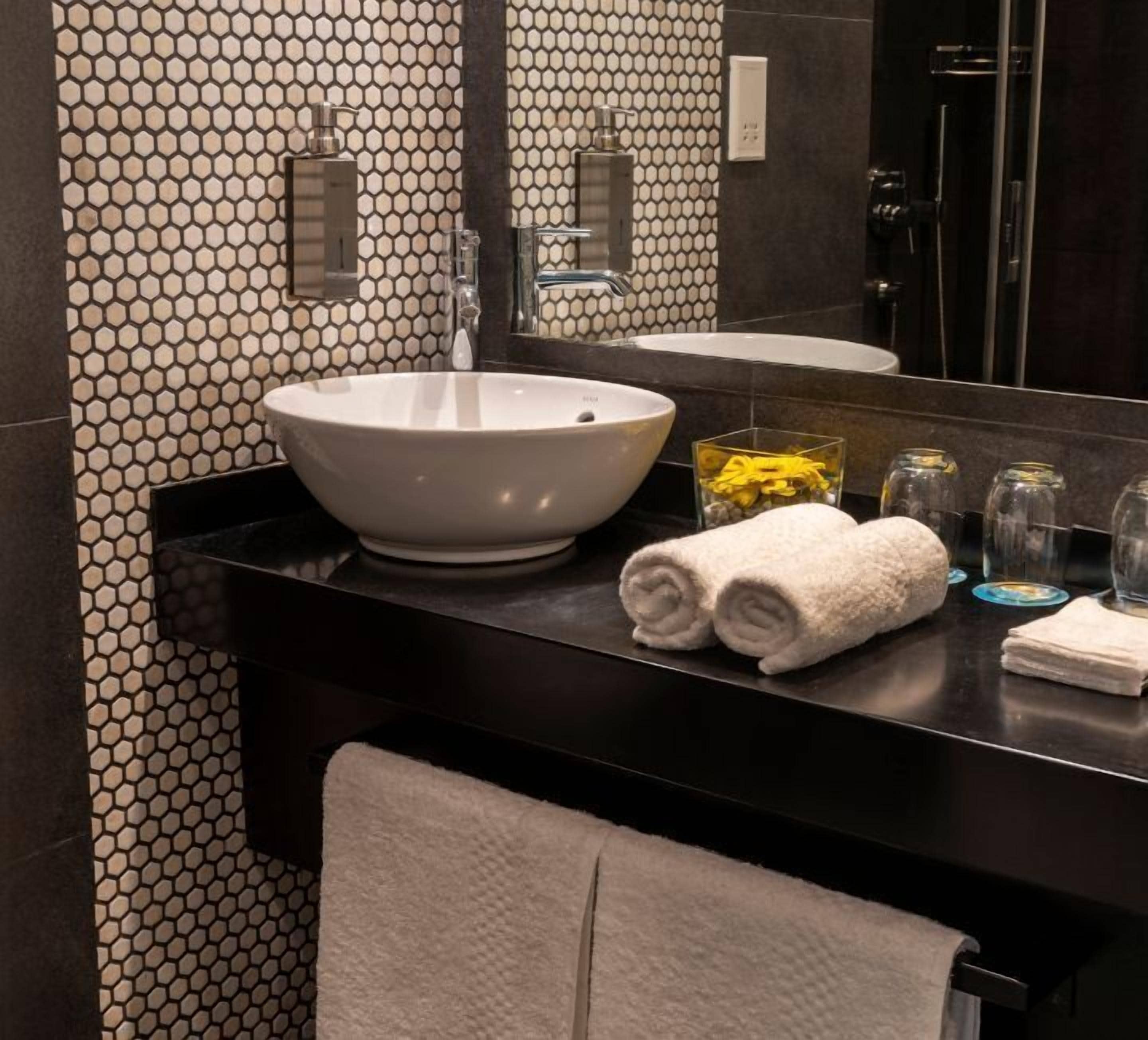 Un baño moderno con un lavabo de pedestal grande, un espejo y una encimera negra.