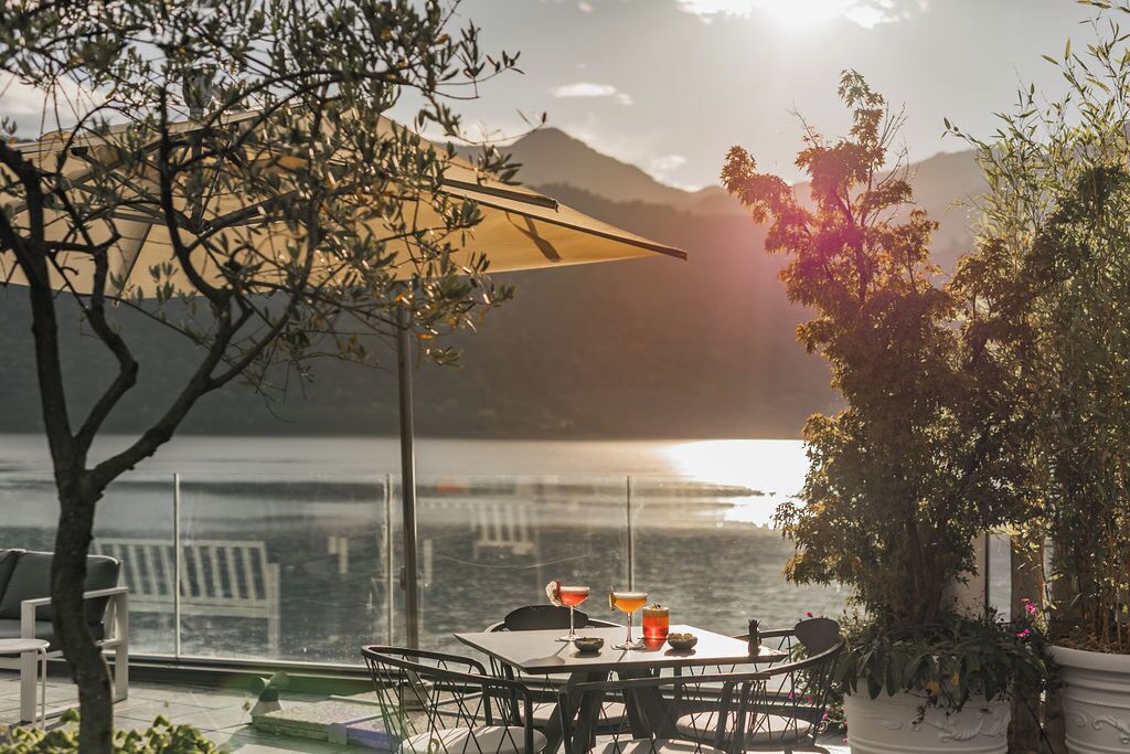 A table with chairs and a table umbrella overlooking a body of water with mountains in the background.