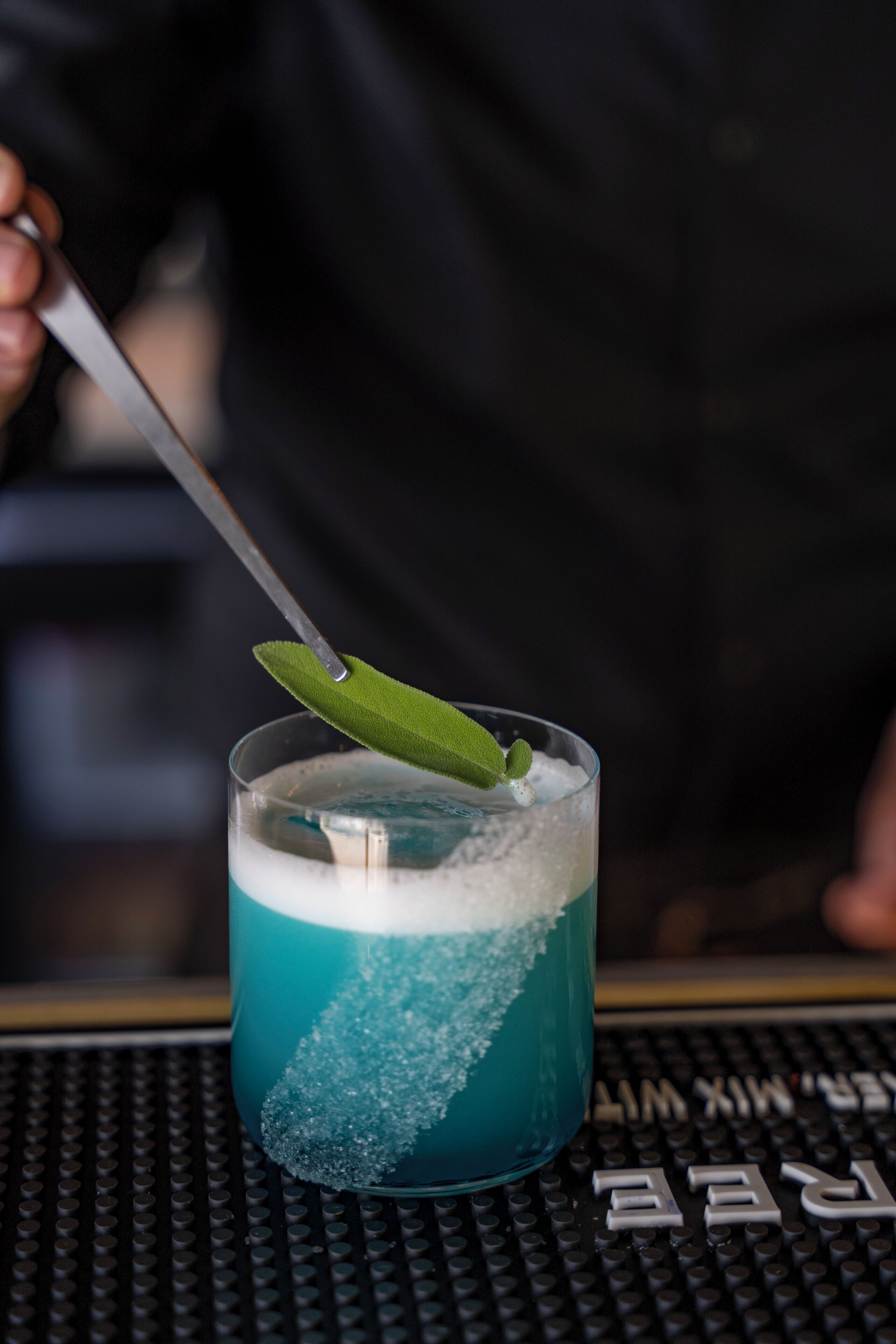 Un cocktail agrémenté d’une feuille verte et servi avec une cuillère dans un verre à la surface texturée.