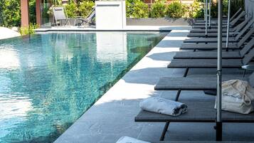 Un espace aménagé au bord de la piscine, avec des chaises longues, un coin salon abrité et une piscine.