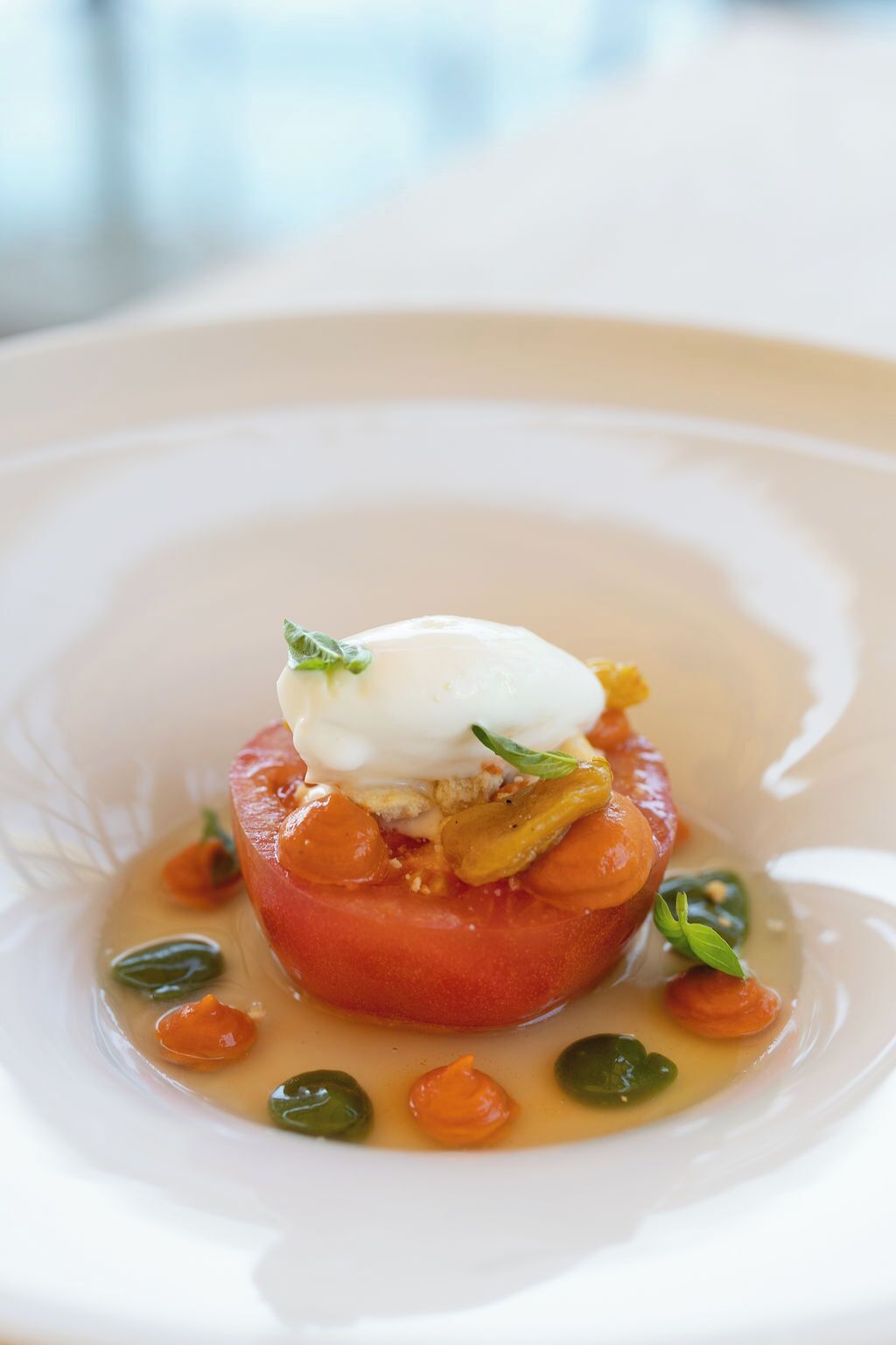 A dish with a poached egg on top of a tomato slice, surrounded by a creamy sauce and garnished with herbs.