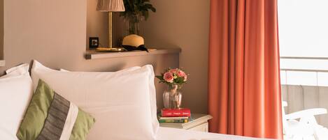 A neatly made bed with pillows, a bedside table with a lamp, books, and a vase of flowers.