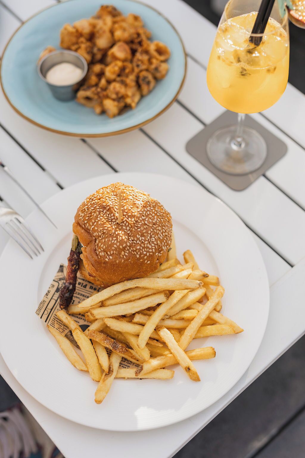 Une assiette avec un hamburger et des frites, un bol de macaronis au fromage et une boisson avec une paille.