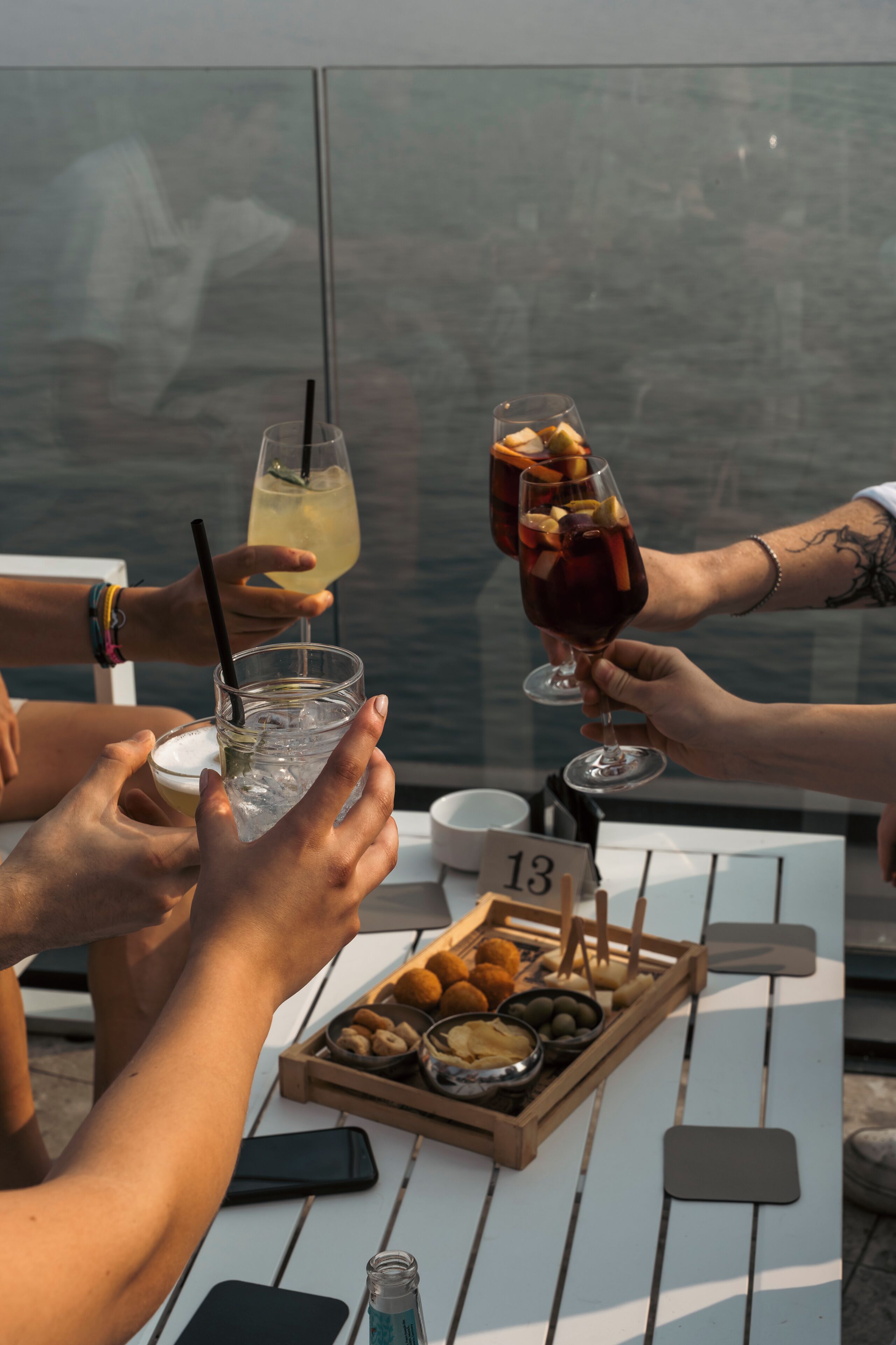 Um grupo de pessoas brindando com bebidas à mesa, com vista para a água.