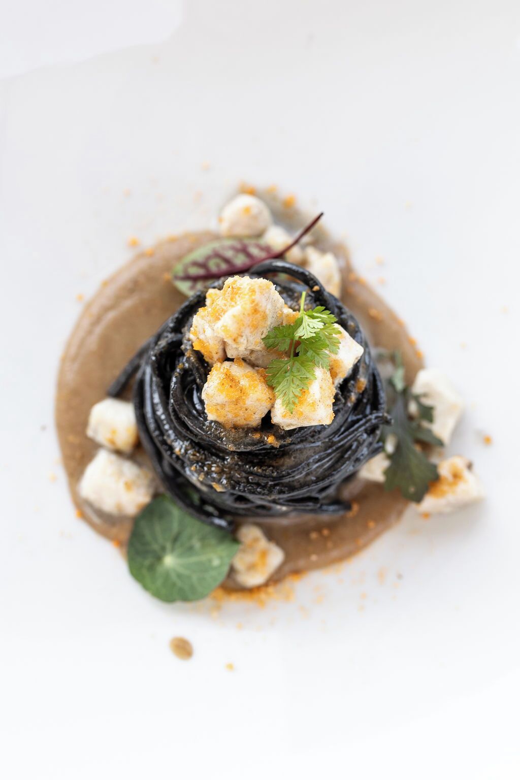 A dish with black noodles, crumbled cheese, and garnishes on a white plate.