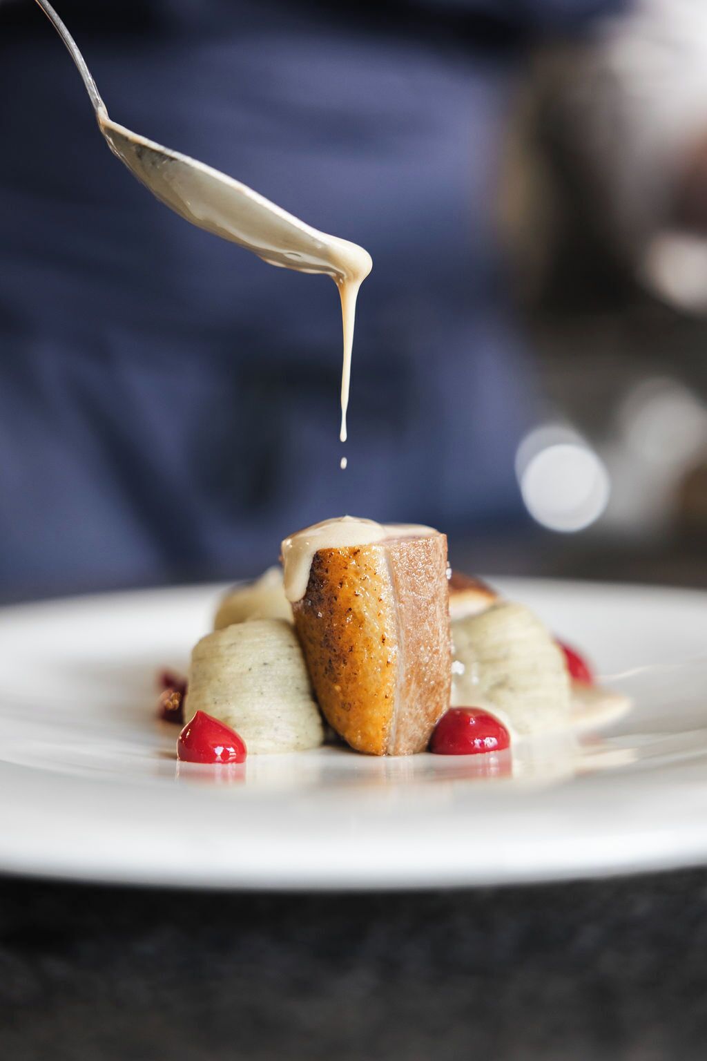 A spoonful of sauce being poured over a dessert on a plate.