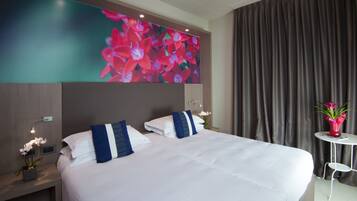 A hotel room with a large bed, two pillows, a nightstand with a lamp, a small table with a vase, and a wall-mounted TV displaying flowers.