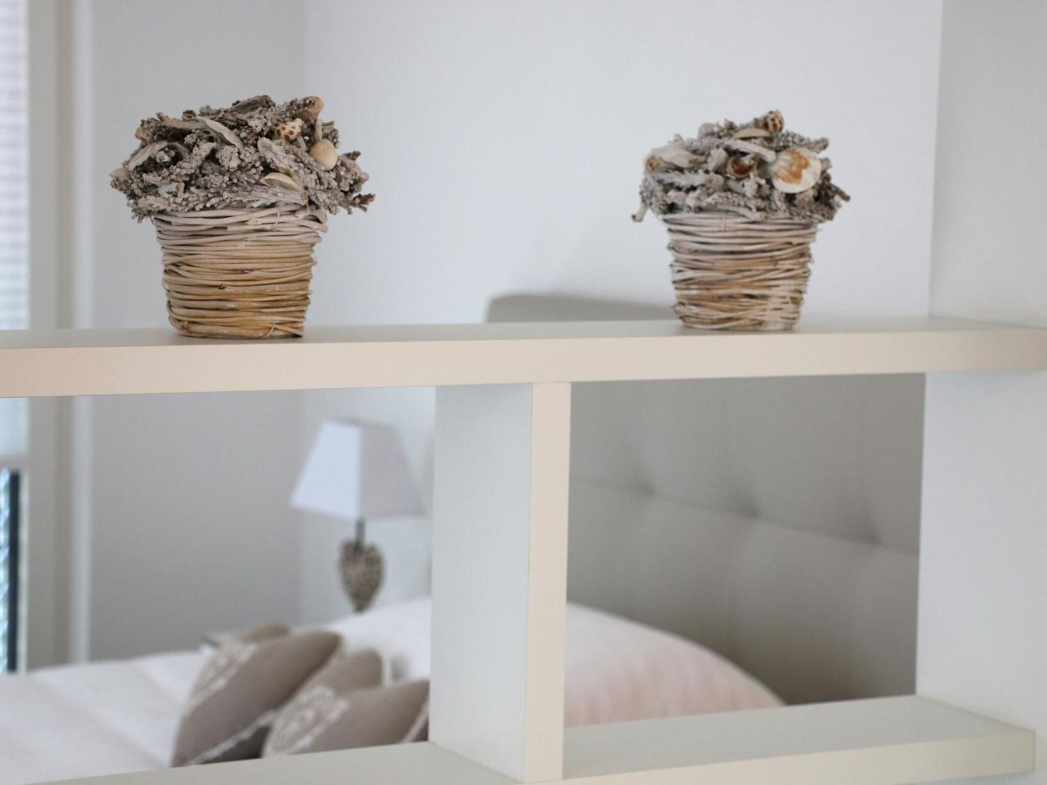 Two wicker baskets with dried flowers and shells on a white shelf.