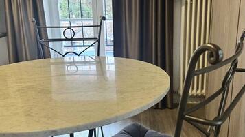 Una mesa redonda con una silla acolchada en una habitación con ventana y cortinas.