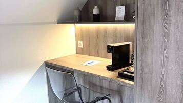 A compact kitchenette with a wooden countertop, a black chair, and a coffee machine.