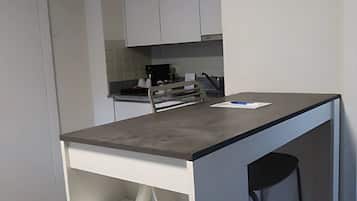 A compact kitchen with white cabinets, a dark countertop, and a bar stool.