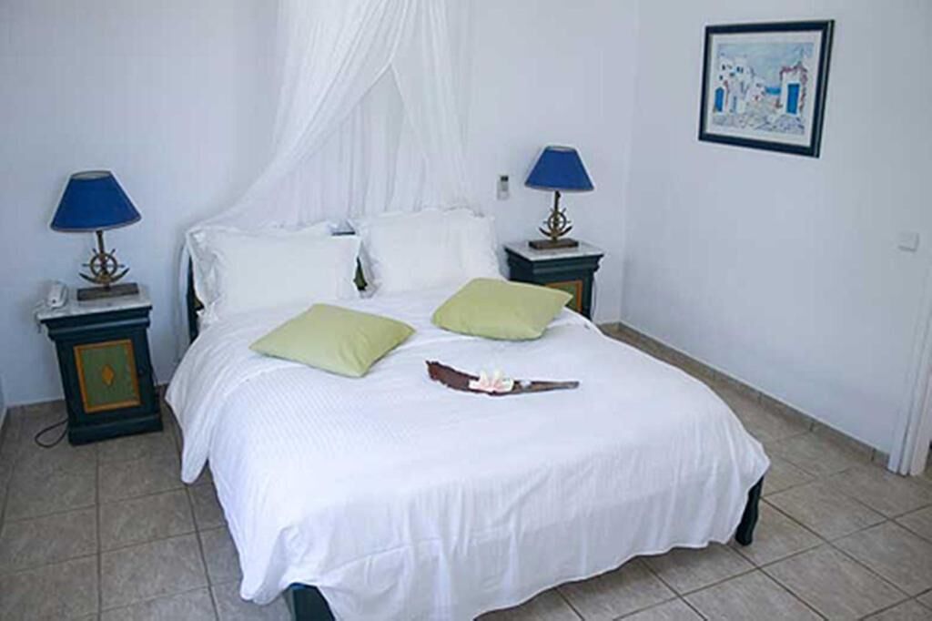 A bed with a white bedspread, two green pillows, a white canopy, and two bedside tables with lamps.