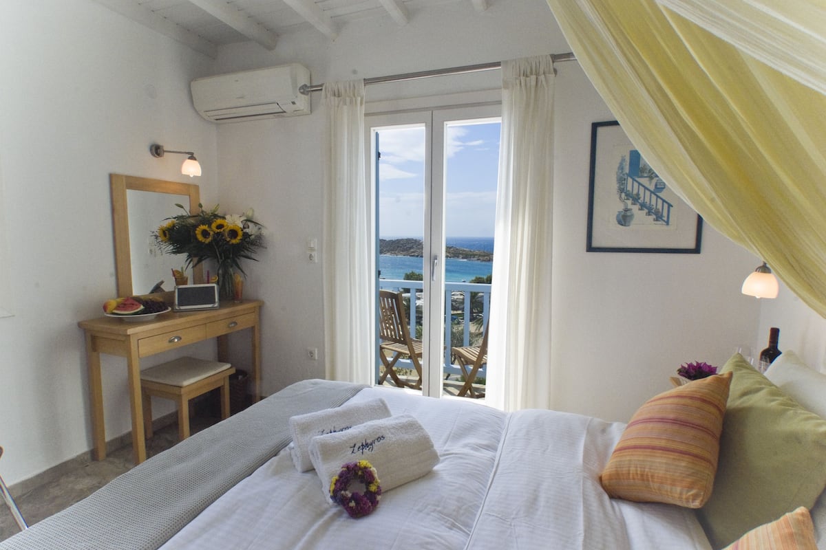 Un dormitorio con cama, escritorio, silla, espejo y vista al mar.