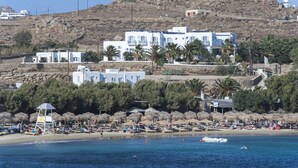 Una zona costera con edificios blancos, una playa con sombrillas y una ladera rocosa.