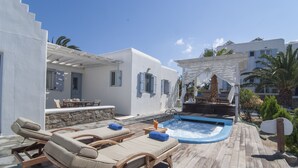 Una terraza de madera con sillones de descanso, un jacuzzi y un muro de piedra.