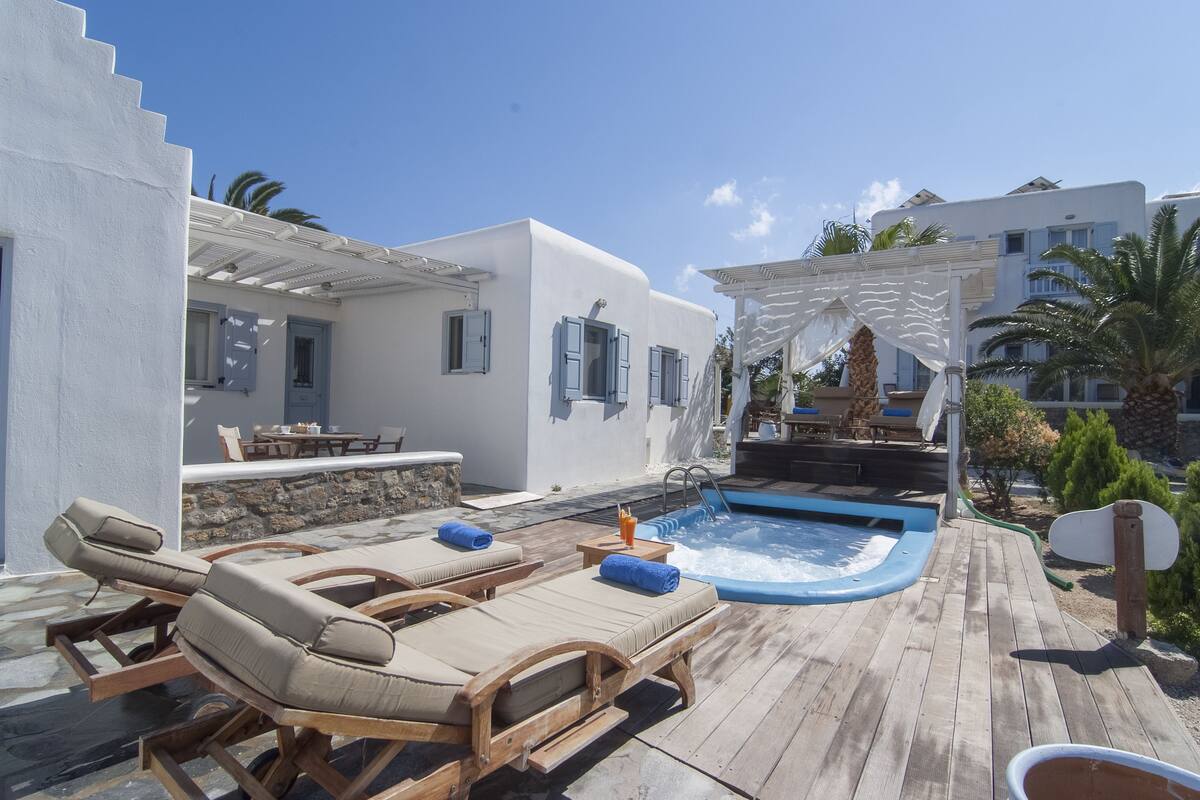 Una terraza de madera con sillones de descanso, un jacuzzi y un muro de piedra.