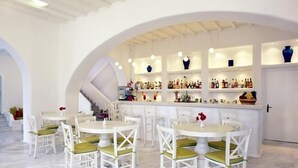 Un restaurante con mobiliario blanco y una zona de bar con estantes llenos de botellas.