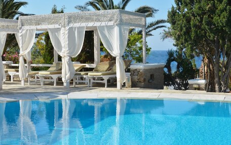 A pool area with a white gazebo, lounge chairs, and a view of the sea.