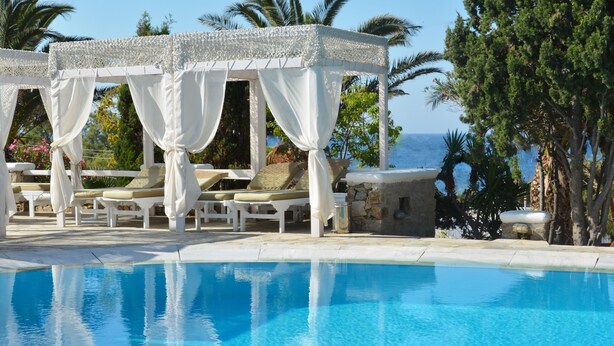 Zona de piscina con un quiosco blanco, sillas de descanso y vista al mar.