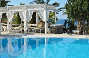 A pool area with a white gazebo, lounge chairs, and a view of the sea. - Zephyros Hotel (Mykonos)